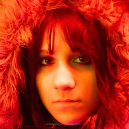 trybmanualny.pl - Portret młodej kobiety o intensywnym spojrzeniu, z czerwonymi włosami i futrzanym kapturem, oświetlony ciepłym, pomarańczowym światłem, z odbiciami w oczach.