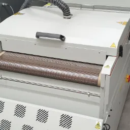 Maszyna DTF z podajnikiem taśmowym i systemem wentylacji, widoczne ostrzeżenia na obudowie.