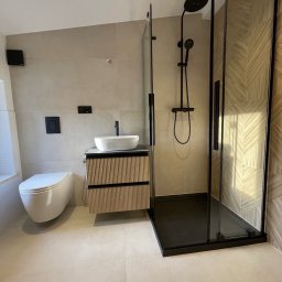 KG-Remonty wykończenia wnętrz Krzysztof Górowski - Nowoczesna łazienka z beżowymi płytkami, kabiną prysznicową typu walk-in z czarnymi elementami i umywalką nablatową na szafce z lamelami. Minimalistyczny design.