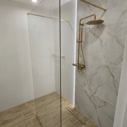 KG-Remonty wykończenia wnętrz Krzysztof Górowski - Kabina prysznicowa walk-in z złotą armaturą i odpływem liniowym, wykończona płytkami imitującymi marmur i drewno. Realizacja w Nowym Sączu.