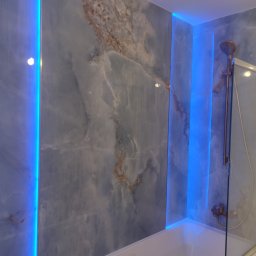 Artiwio Sp. z o.o. - Wykończona łazienka z marmurowymi płytkami, podświetleniem LED i miedzianą armaturą prysznicową za szklanym panelem.