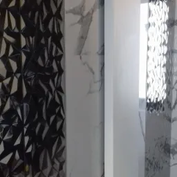 Fragment ściany z różnorodnymi płytkami: czarne lustrzane z geometrycznym wzorem, białe marmurowe oraz białe gładkie, oddzielone pionowymi pasami.