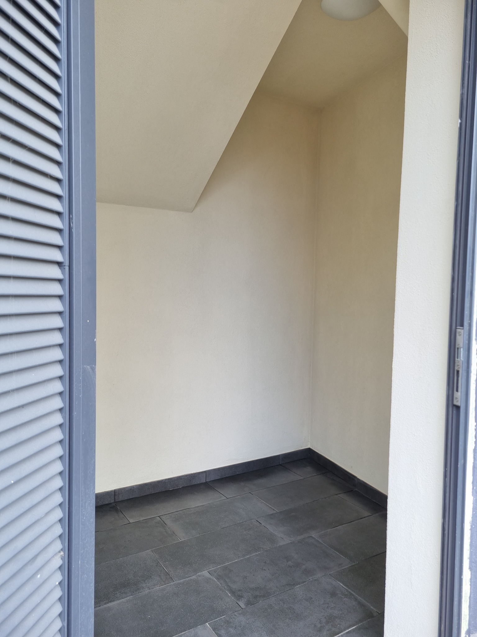 Wnęka z szarymi płytkami podłogowymi, widok zza szarych drzwi z żaluzjami, Gorzów Wielkopolski.