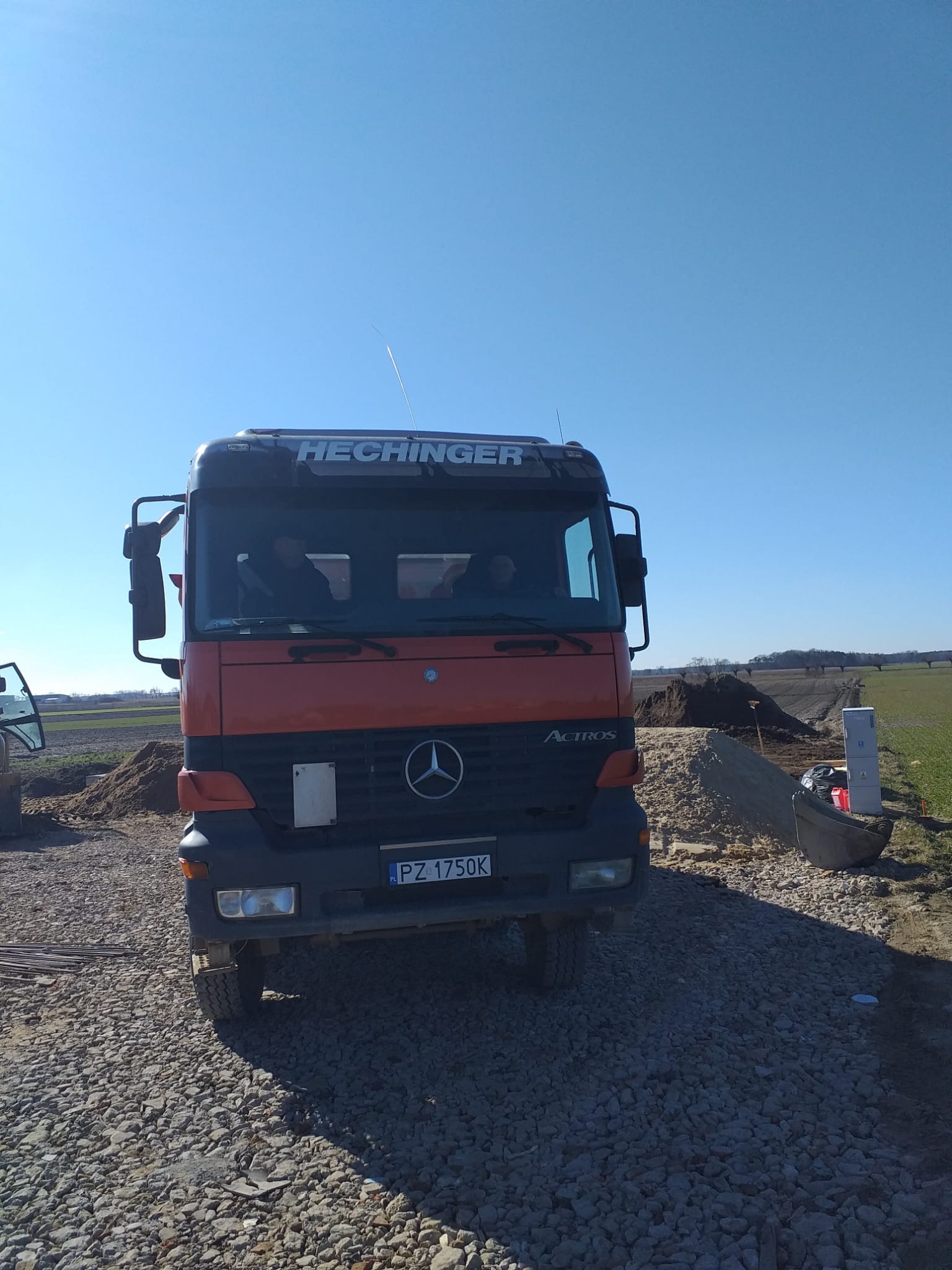 Ciężarówka marki Hechinger Actros na placu budowy, widoczne wykopane podłoże i elementy instalacji elektrycznej.