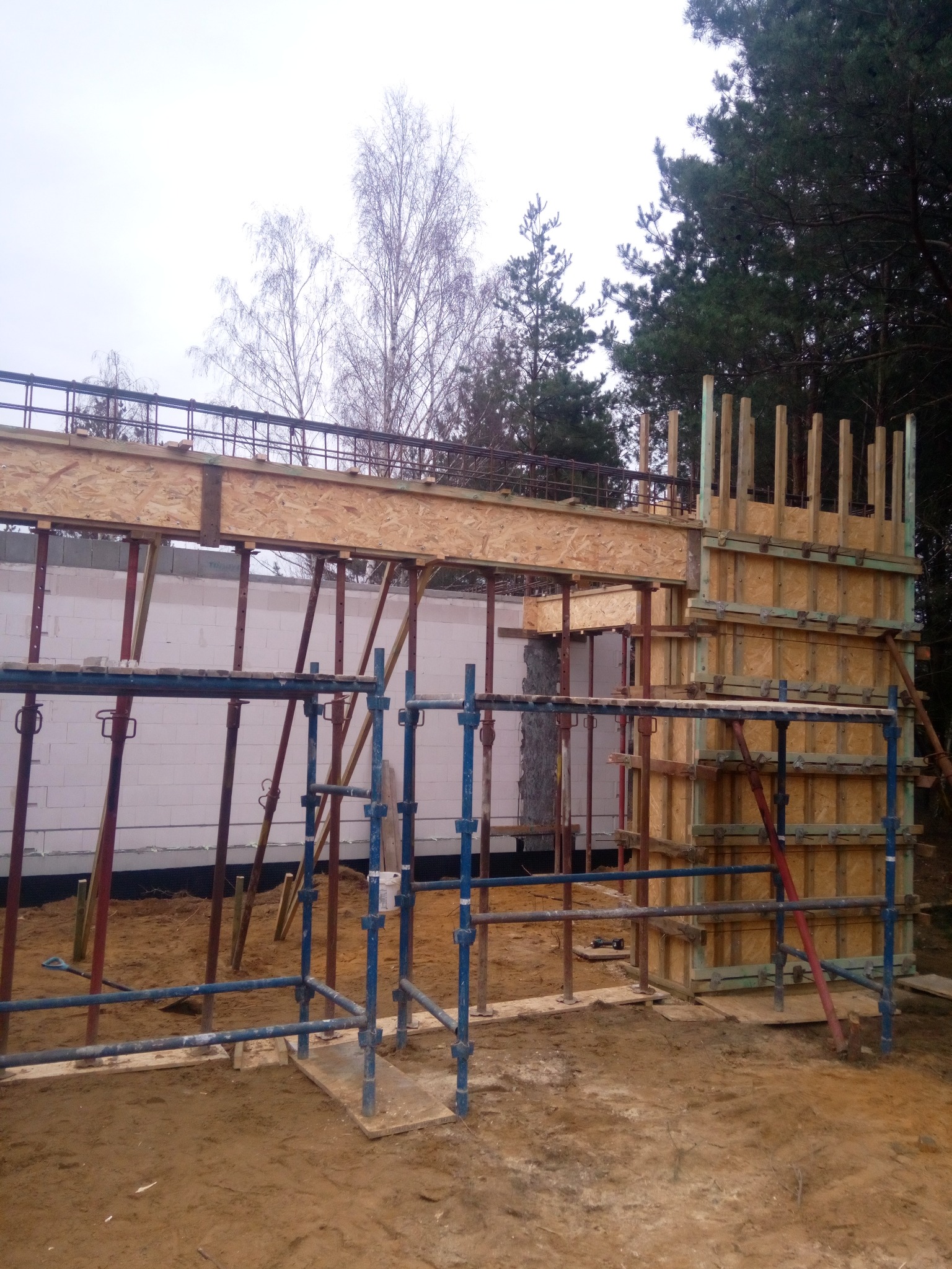 Szczegółowe ujęcie szalunków z desek i podpór, przygotowanych do wylania betonu na budowie, z widocznym zbrojeniem i fragmentem ściany z bloczków.