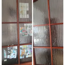 Drewniane drzwi z szybą, na której przyklejone są obrazki z postaciami z bajek, wykonane z pociętych kartek, niektóre z nich częściowo odklejone.