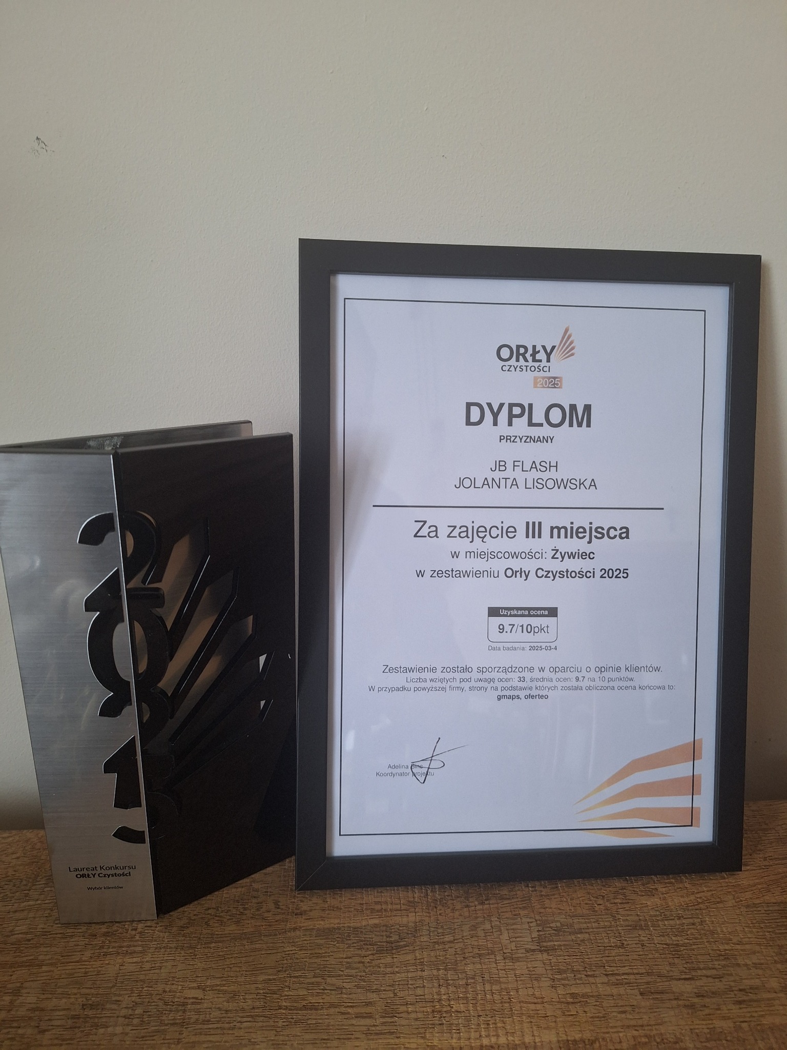 Dyplom i statuetka 'Orły Czystości 2025' za zajęcie III miejsca, przyznane firmie JB Flash, Jolanta Lisowska, z oceną 9.7/10, na drewnianym blacie.