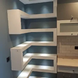 Narożna, podświetlana półka z płyty karton gips w nowoczesnej kuchni, zintegrowana z zabudową meblową i oświetleniem punktowym.