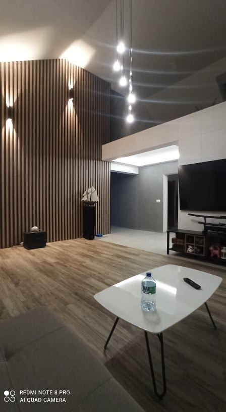 Nowoczesny salon z drewnianą ścianą lamelową, białym stolikiem kawowym z butelką wody i wiszącymi lampami punktowymi.