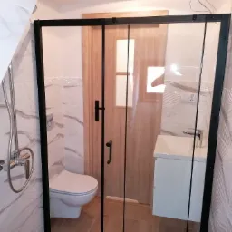 Nowoczesna kabina prysznicowa z czarnymi profilami w łazience w Trzebielinie, widoczna umywalka z szafką, toaleta i armatura prysznicowa na tle marmurowych płytek.