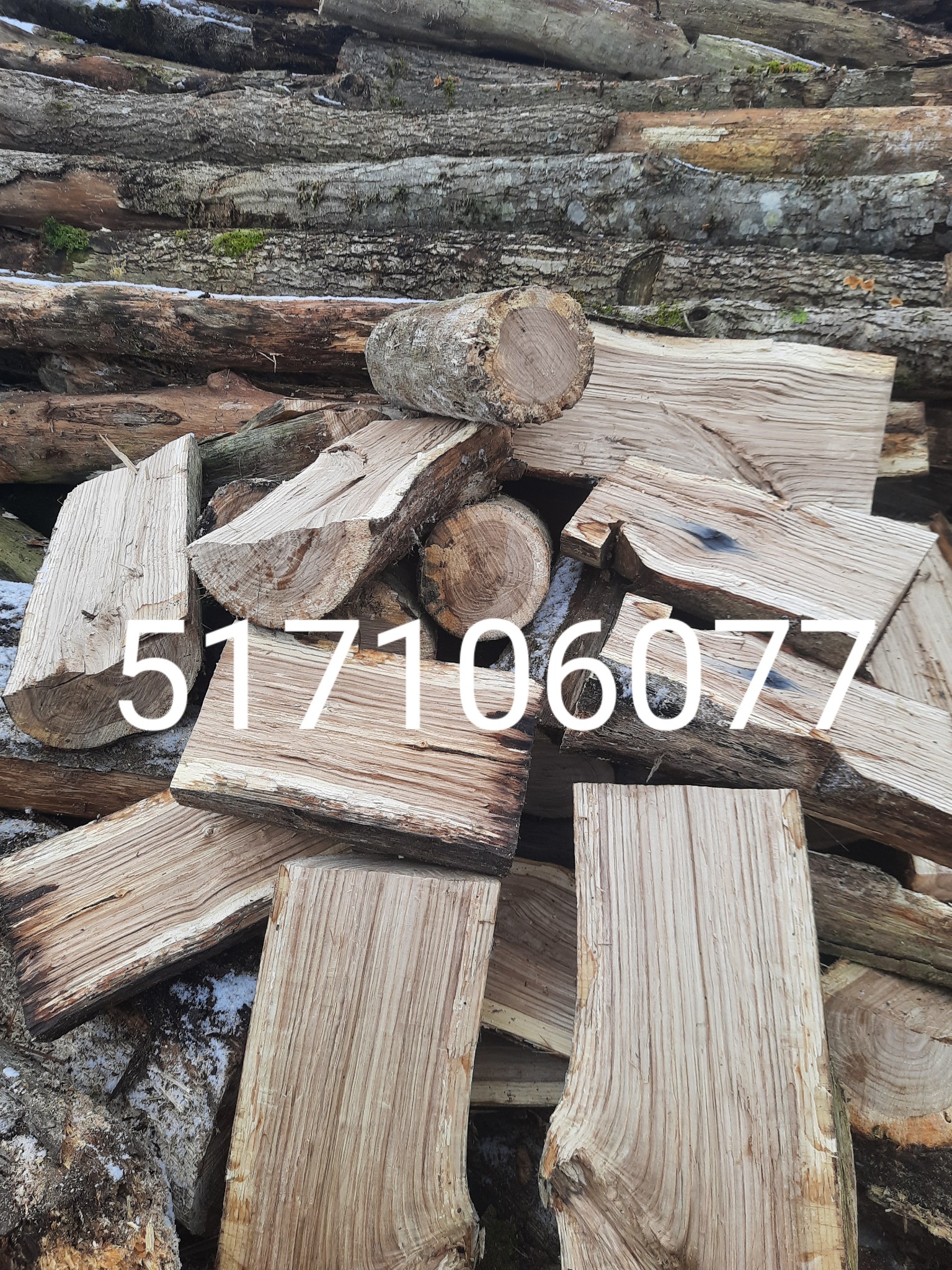 Stos pociętego drewna z widocznym numerem telefonu nałożonym na zdjęcie, w tle kora i resztki śniegu.