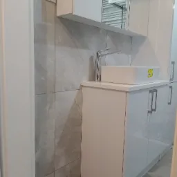 Nowoczesna łazienka z białą szafką pod umywalką, prostokątną umywalką nablatową, chromowaną baterią i szarą marmurową ścianą.