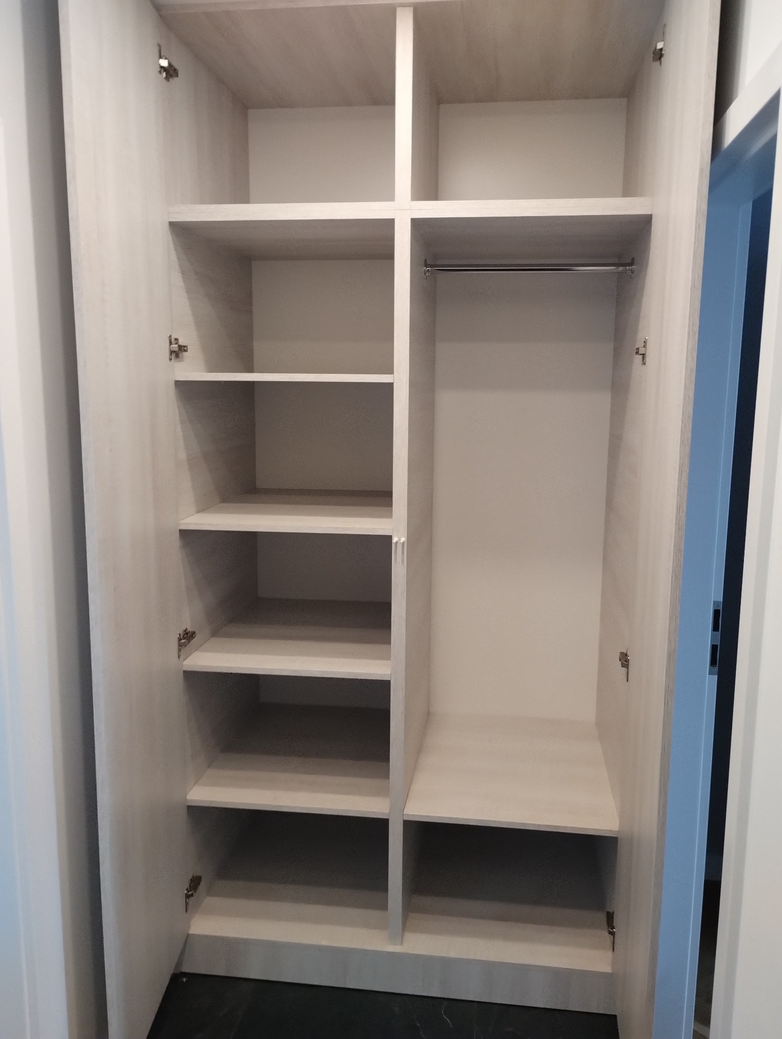 Wnętrze jasnej, otwartej szafy wnękowej z półkami po lewej stronie i drążkiem na ubrania po prawej, widok z przodu, ciemna podłoga.