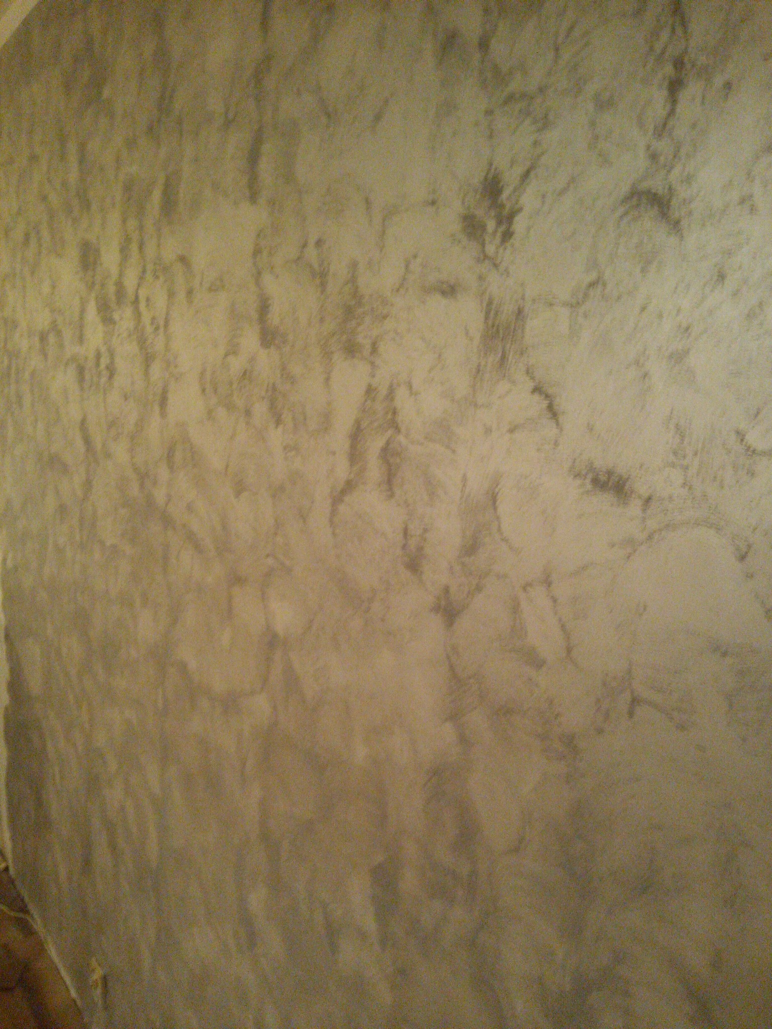 Ściana pokryta dekoracyjną, szarobeżową gładzią strukturalną z efektem cieniowania, prezentująca nieregularne wzory i fakturę.