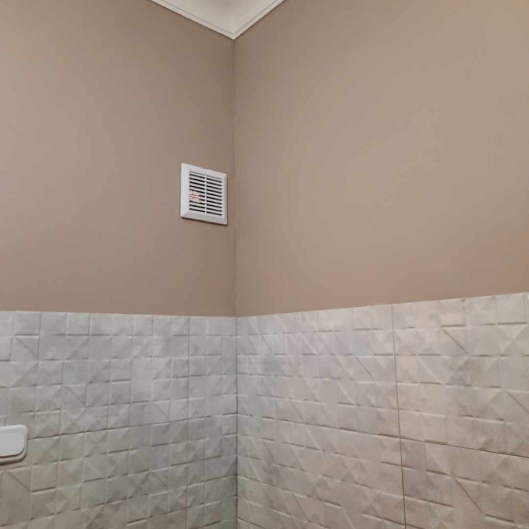 Wykończona łazienka z beżową ścianą, białymi trójwymiarowymi płytkami i kratką wentylacyjną w rogu, widok z dołu.