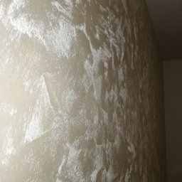 DAS the art of real estate sp. zo.o. - Ściana pokryta dekoracyjną, perłową farbą strukturalną w odcieniach beżu i srebra, z widoczną fakturą i efektem odbijania światła.