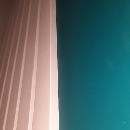 DAS the art of real estate sp. zo.o. - Fragment ściany pomalowanej na intensywny turkusowy kolor, sąsiadującej z dekoracyjną, pionową boazerią w odcieniach bieli i beżu, widzianej pod kątem.