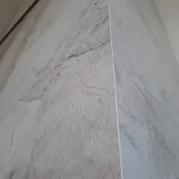 Wewnętrzny narożnik wykończony płytami imitującymi marmur, z widoczną listwą narożną i fragmentem sufitu z czarną linią wentylacyjną.