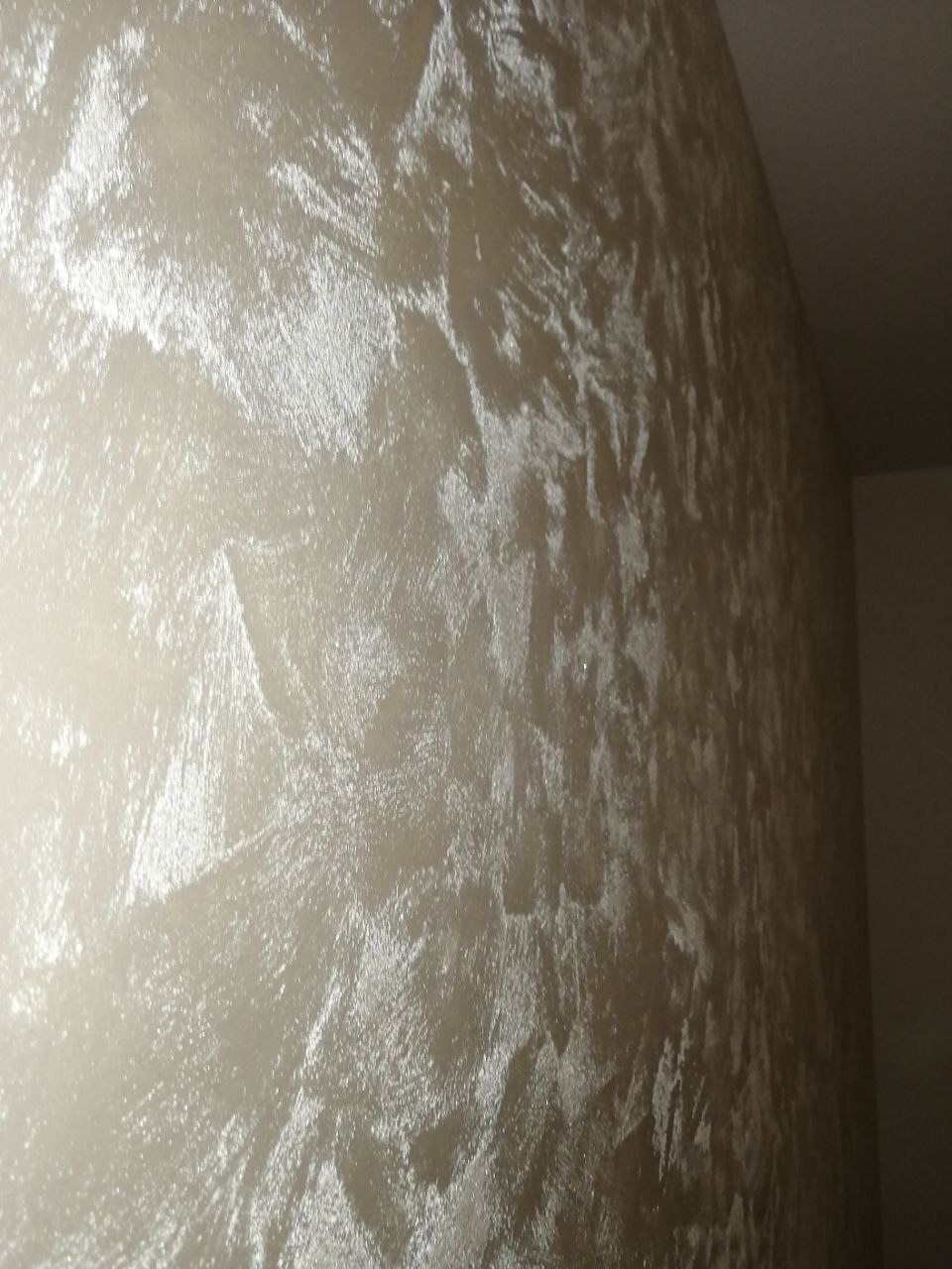 Ściana pokryta dekoracyjną, perłową farbą strukturalną w odcieniach beżu i srebra, z widoczną fakturą i efektem odbijania światła.