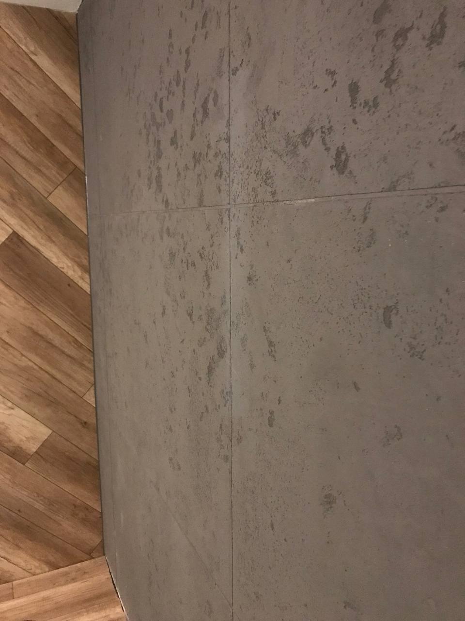 Szare, matowe płytki ścienne z efektem betonu sąsiadują z podłogą z drewnopodobnych paneli ułożonych w jodełkę.