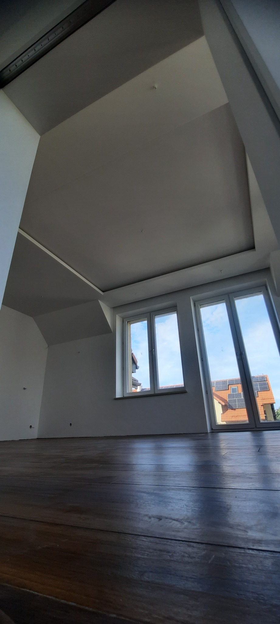 Poddasze z wykończonym sufitem, drewnianą podłogą i oknami z widokiem na dom z panelami słonecznymi.