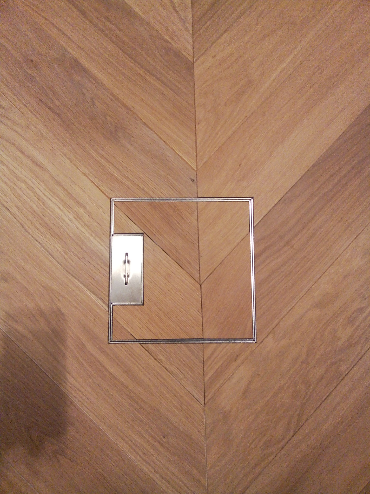 Parkiet ułożony we wzór jodełki francuskiej w Gdańsku, z widoczną metalową klapą rewizyjną, idealnie wkomponowaną w drewnianą podłogę.