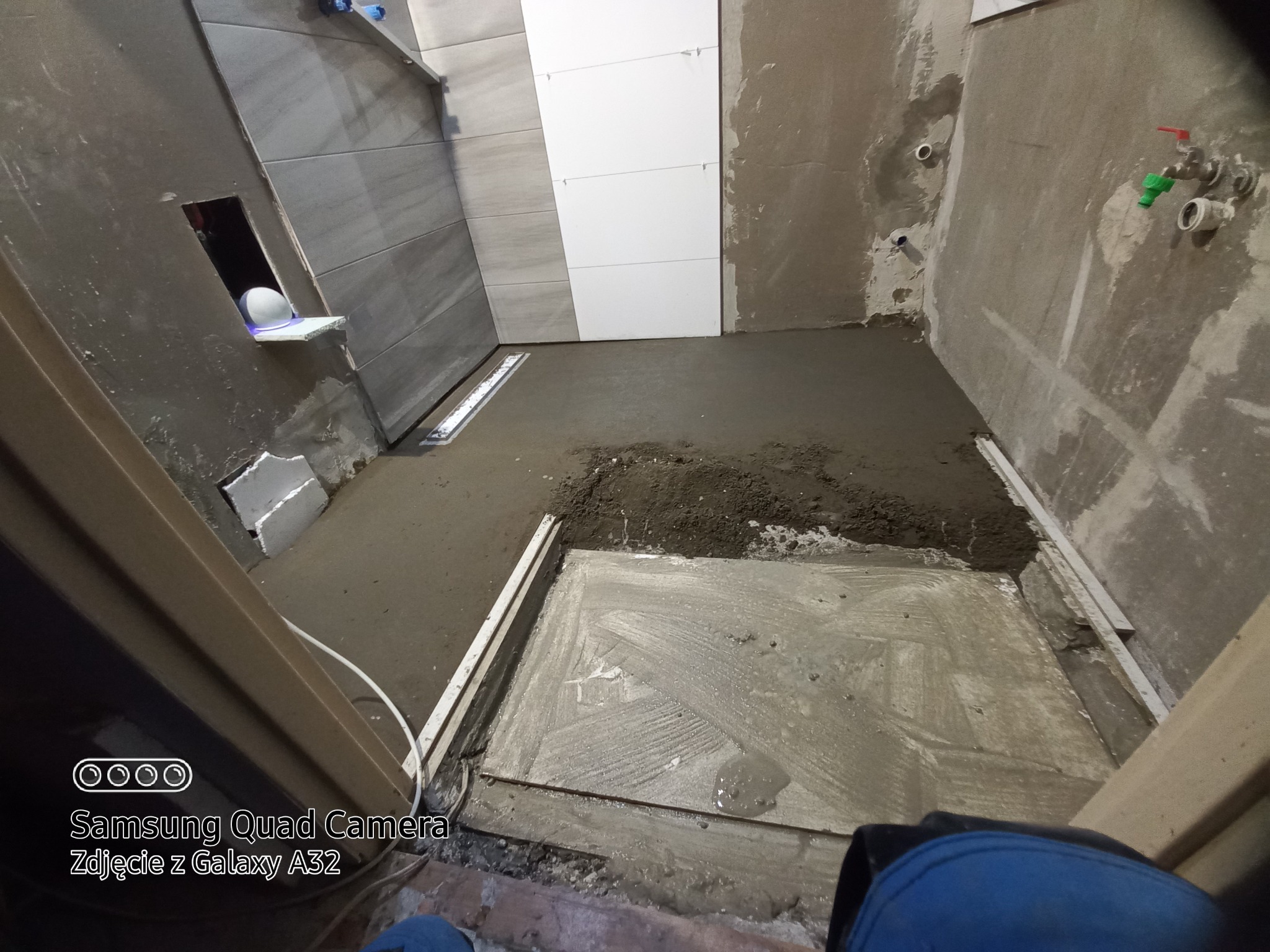 Przygotowanie podłoża pod prysznic w trakcie remontu łazienki: wylewka cementowa, częściowo położone płytki ścienne, widoczne instalacje wodne.