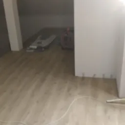 Poddasze z wykończoną podłogą z paneli, widoczne materiały budowlane i kabel elektryczny, w trakcie prac wykończeniowych.