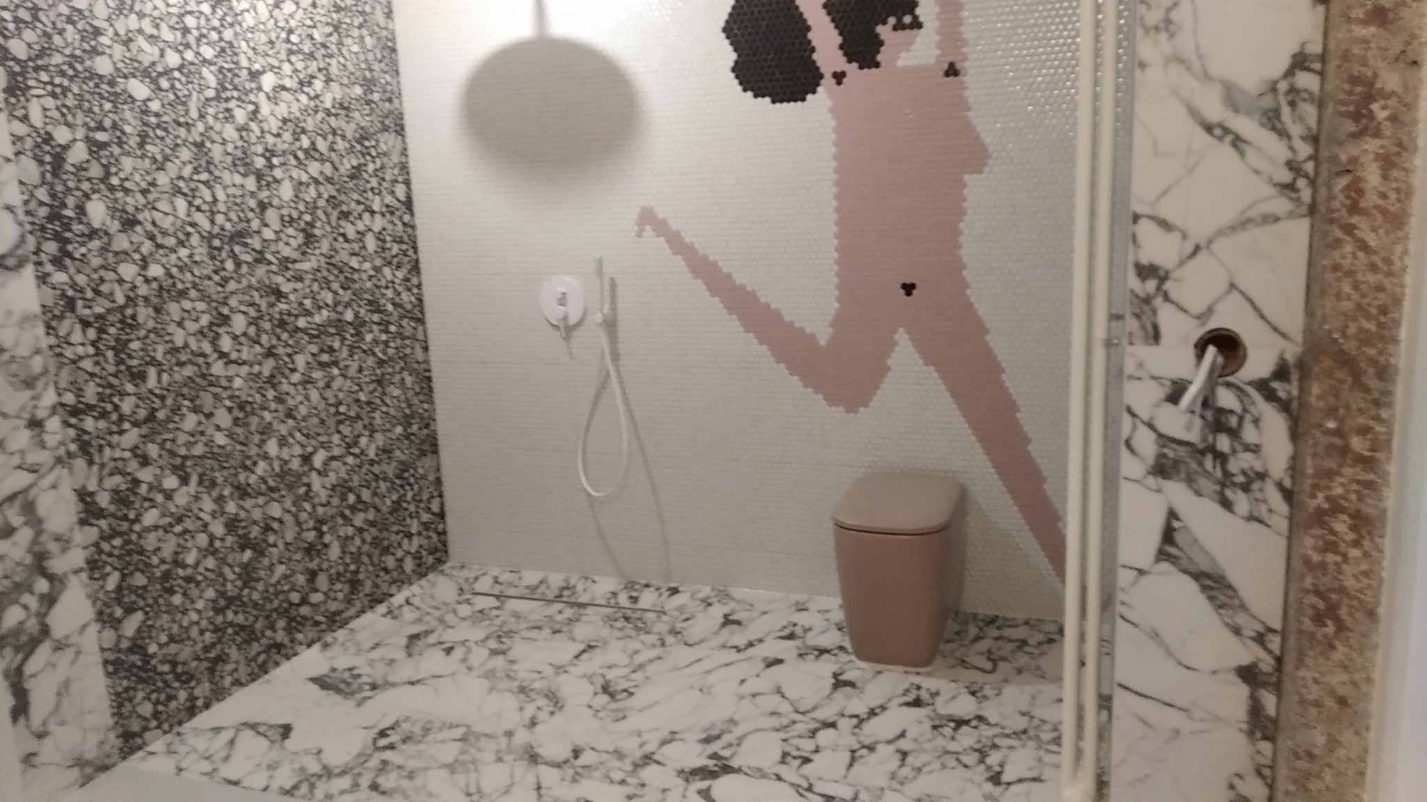 Nowoczesna kabina prysznicowa z mozaiką przedstawiającą postać, marmurową posadzką i ścianą, oraz podtynkową baterią natryskową.