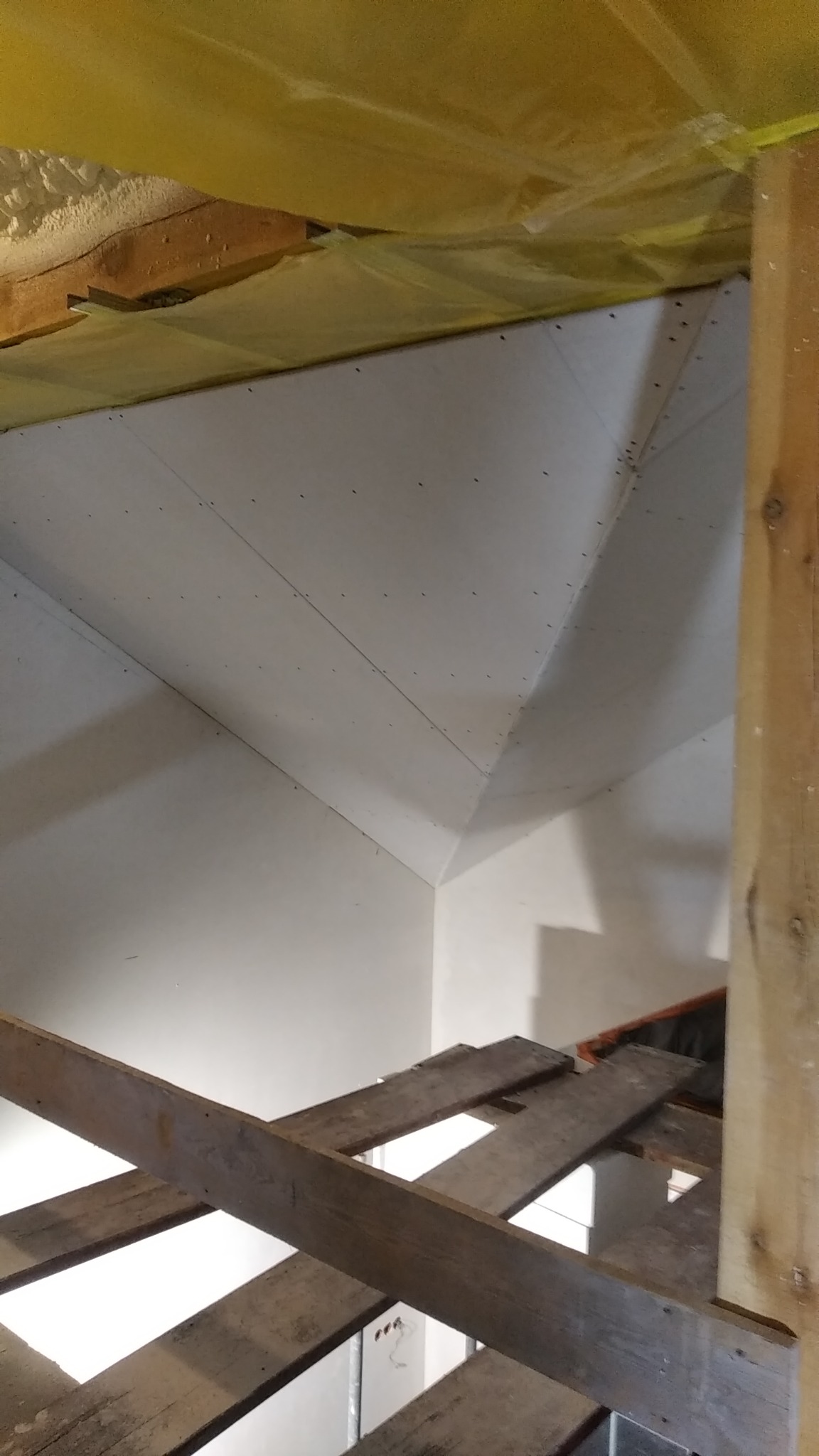 Skośne poddasze z widoczną konstrukcją drewnianą i zamontowanymi płytami gipsowo-kartonowymi, zabezpieczone folią budowlaną, widok z rusztowania.