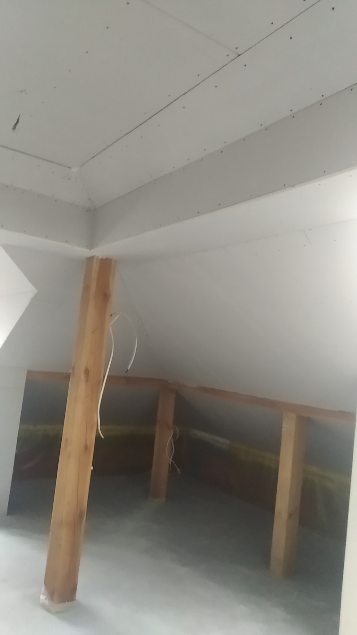 Skośne poddasze z widoczną drewnianą konstrukcją nośną i zamontowanymi płytami gipsowo-kartonowymi, widoczne kable instalacji elektrycznej.