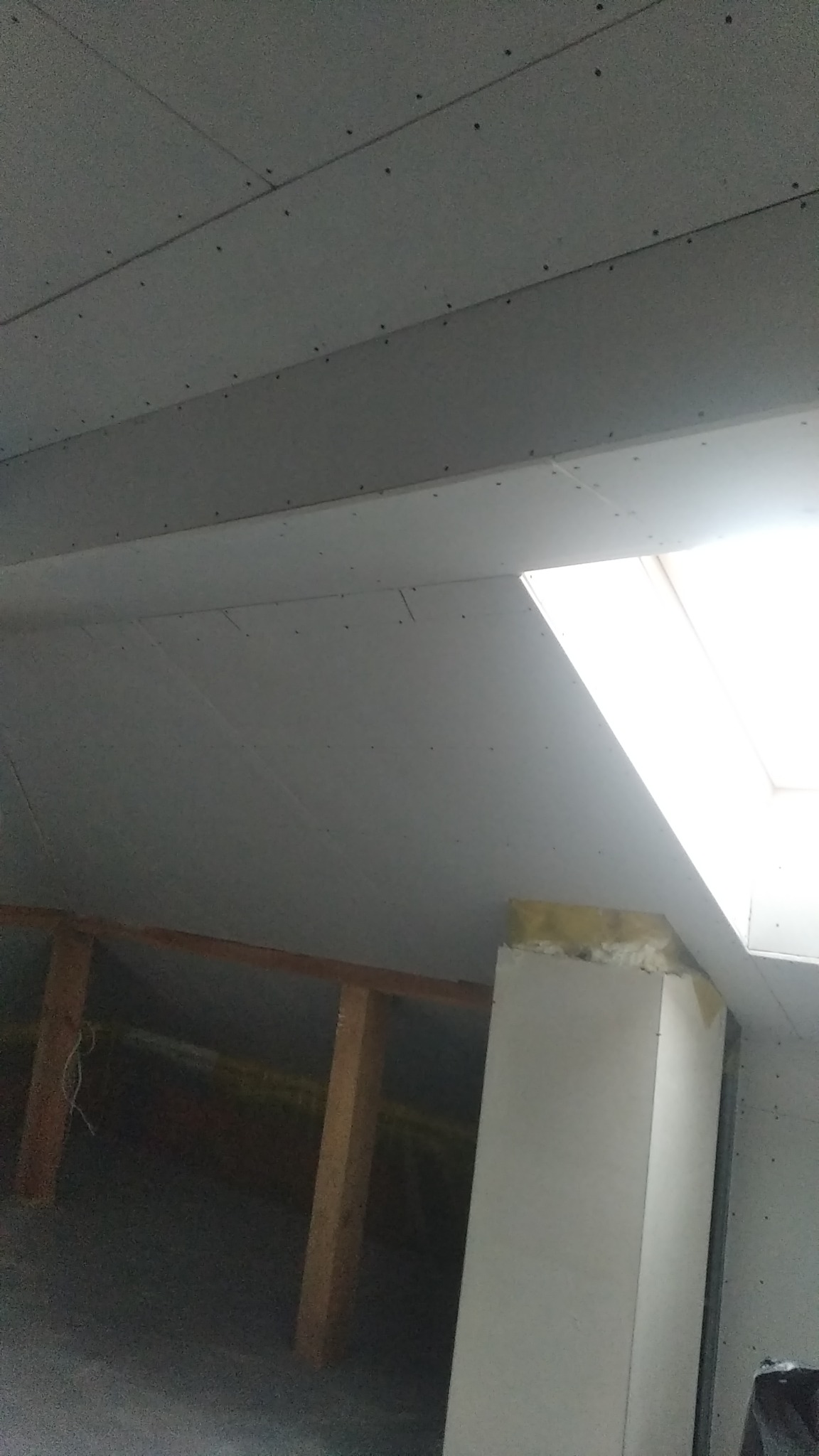 Sufit na poddaszu z zamontowaną płytą gipsowo-kartonową i oknem dachowym, widoczne drewniane elementy konstrukcyjne.