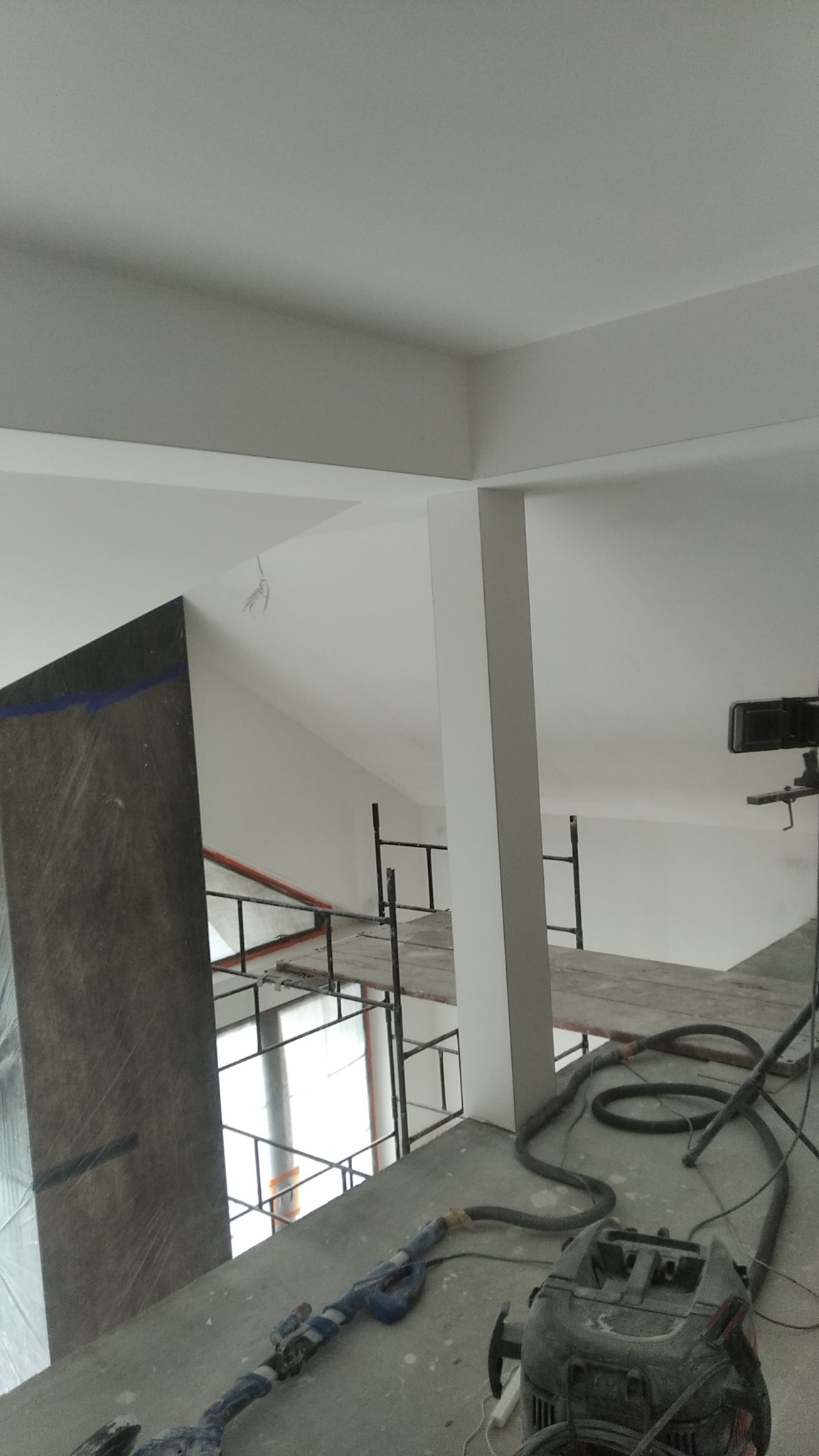Wnętrze w trakcie prac wykończeniowych: szlifierka do gładzi, odkurzacz przemysłowy, rusztowanie, przygotowana ściana z płyt kartonowo-gipsowych.