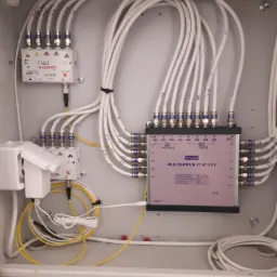 Rozdzielacz multiswitch TT 9/12 FT w skrzynce instalacyjnej z podłączonymi kablami koncentrycznymi i zasilaczem, widoczne napisy Hot Bird i Astra.