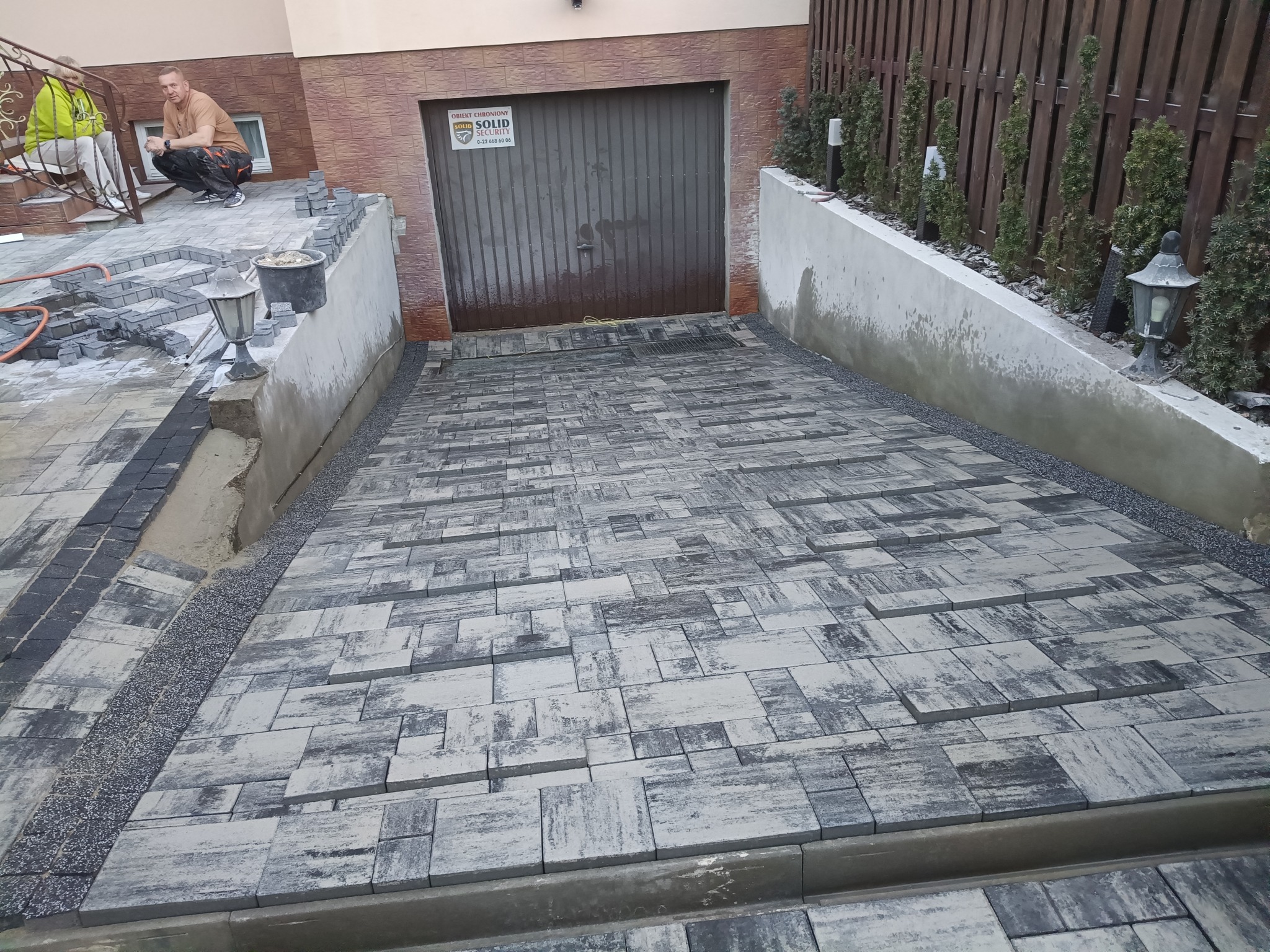 Ułożona kostka brukowa prowadząca do garażu, z widocznymi elementami w trakcie prac. Mężczyzna przy pracy.
