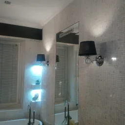 Nowoczesna łazienka z wolnostojącą wanną, baterią podłogową i ścianami wyłożonymi mozaiką, oświetlona kinkietami z czarnymi abażurami i podświetlanymi półkami z dekoracjami.