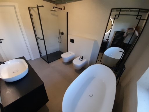 Nowoczesna łazienka z czarnymi akcentami: kabina prysznicowa typu walk-in, umywalka nablatowa na czarnej szafce, wolnostojąca wanna i bidet, całość dopełniona dużym lustrem.