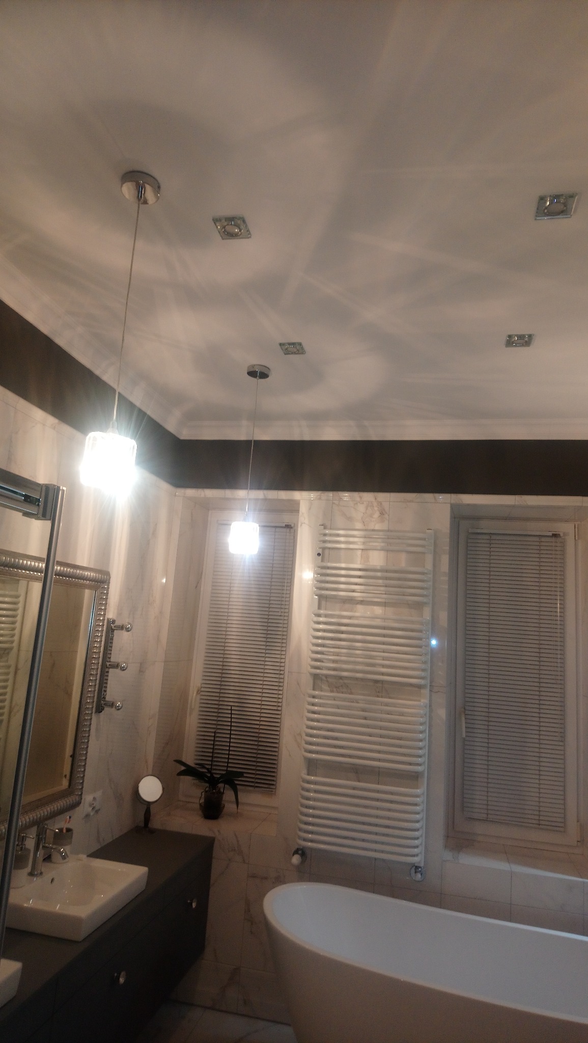 Nowoczesna łazienka z marmurowymi płytkami, wiszącymi lampami z kwadratowymi kloszami, grzejnikiem drabinkowym i owalną wanną wolnostojącą.