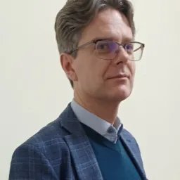 Portret mężczyzny w okularach i marynarce w kratę na jasnym tle. Uśmiechnięty, z delikatnymi zmarszczkami wokół oczu. Profesjonalny wygląd, idealny na zdjęcie profilowe.