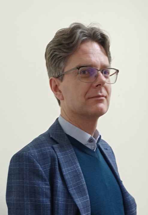 Portret mężczyzny w okularach i marynarce w kratę na jasnym tle. Uśmiechnięty, z delikatnymi zmarszczkami wokół oczu. Profesjonalny wygląd, idealny na zdjęcie profilowe.