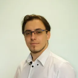 Portret młodego mężczyzny w okularach i białej koszuli na jasnym tle, prawdopodobnie specjalista z Rudy Śląskiej.