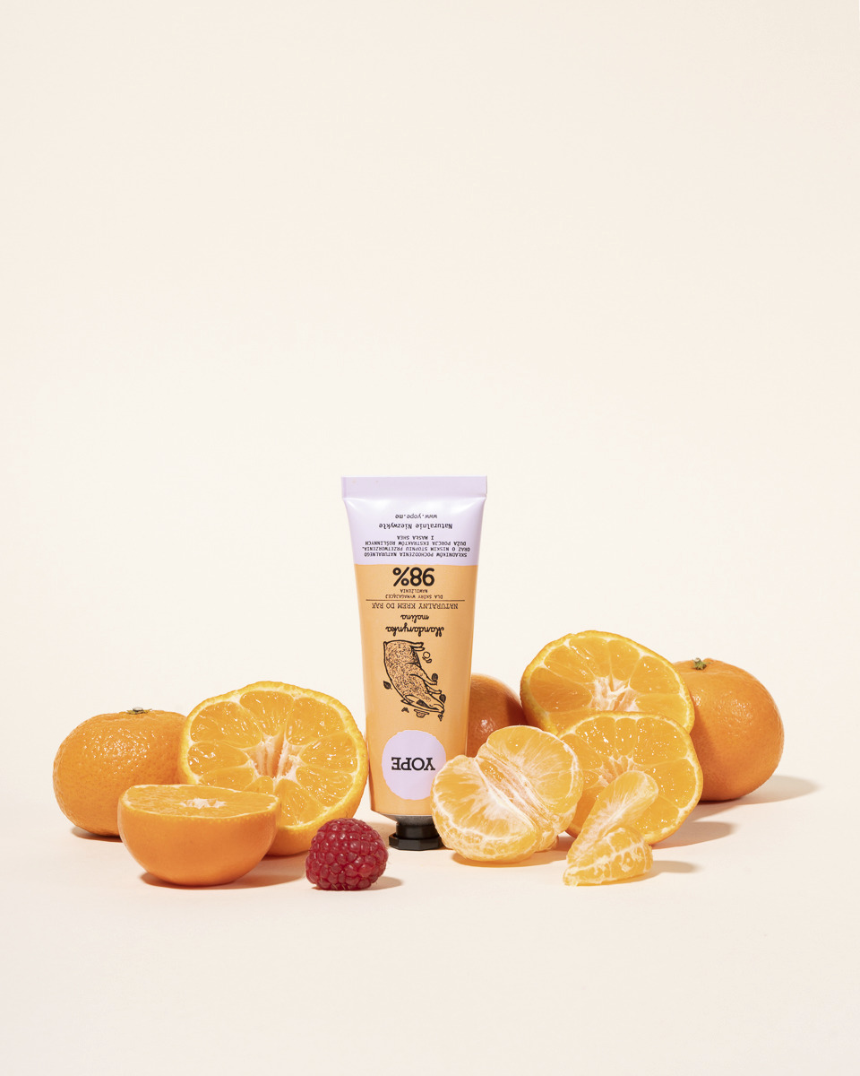 Krem do rąk Yope o zapachu mandarynki i maliny otoczony świeżymi mandarynkami i jedną maliną na jasnym tle.
