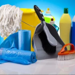 Zestaw środków i akcesoriów do sprzątania: mop, wiadro, worki na śmieci, zmiotka z szufelką, butelki z płynami, gąbki. Ujęcie studyjne na niebieskim tle.