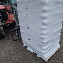 Paleta zafoliowanego pelletu z widocznym logo BK i napisem PREMIUM PELLETS, podnoszona przez ładowarkę teleskopową Manitou na ziemi z liśćmi.