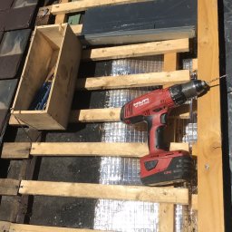 Usługi Stolarskie - Częściowo zdjęte pokrycie dachu z łupka, widoczna drewniana konstrukcja, izolacja, skrzynka z narzędziami i wkrętarka Hilti.