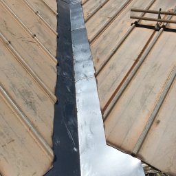 Usługi Stolarskie - Metalowa obróbka komina na dachu z blachy trapezowej w kolorze beżowym, widoczne mocowania rynny