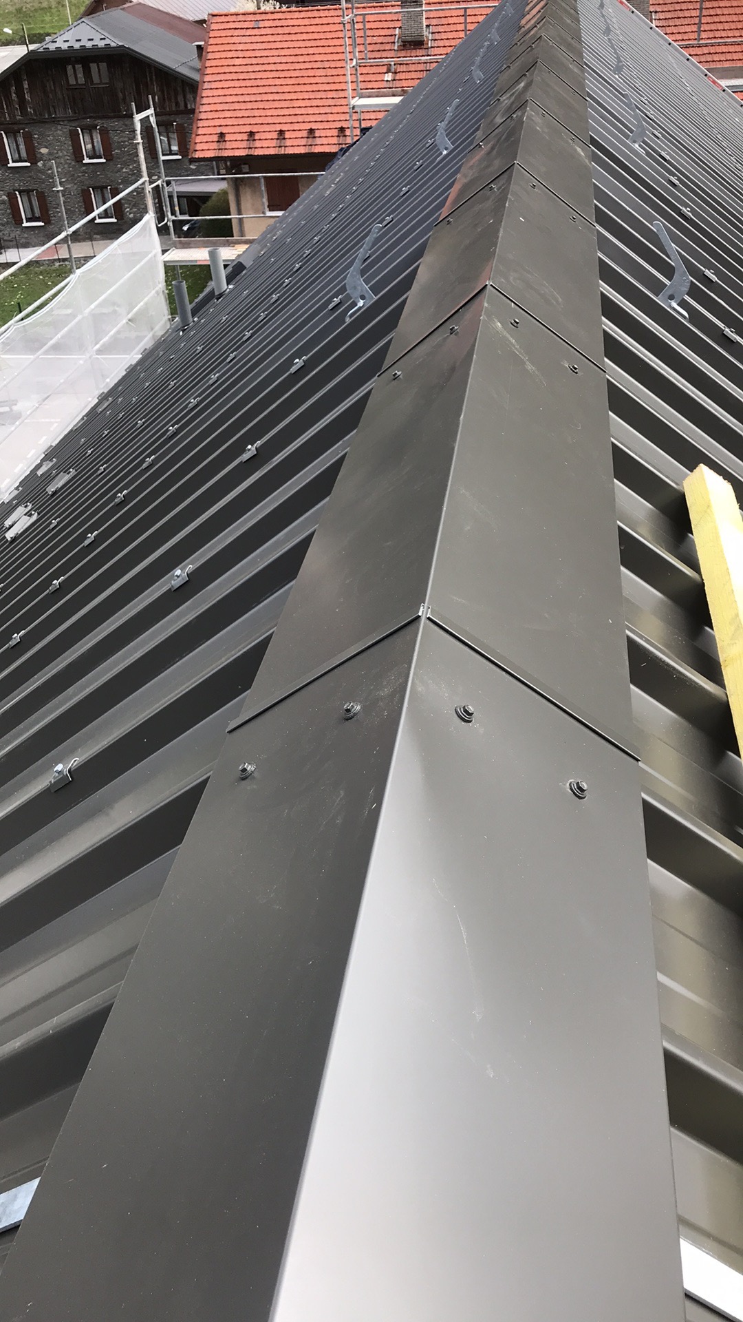 Nowy, ciemnoszary dach z blachy na budynku mieszkalnym, widoczny fragment kalenicy z mocowaniami i elementami wykończeniowymi.