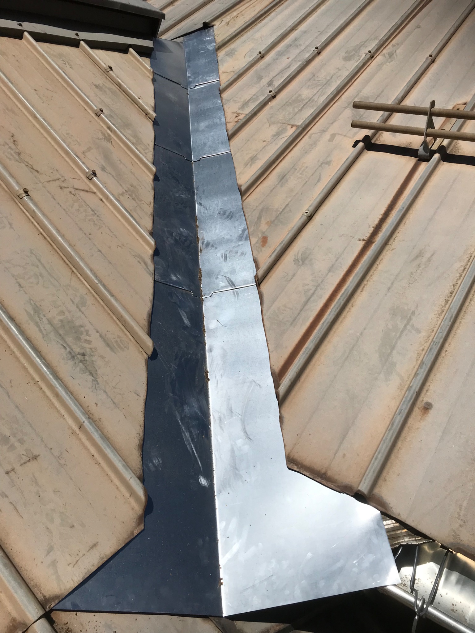 Metalowa obróbka komina na dachu z blachy trapezowej w kolorze beżowym, widoczne mocowania rynny