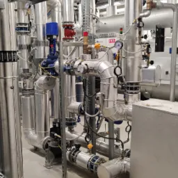 Kompleksowa instalacja rur z zaworami, manometrami i izolacją termiczną w pomieszczeniu technicznym, widoczne rury z oznaczeniami GLYCOL.
