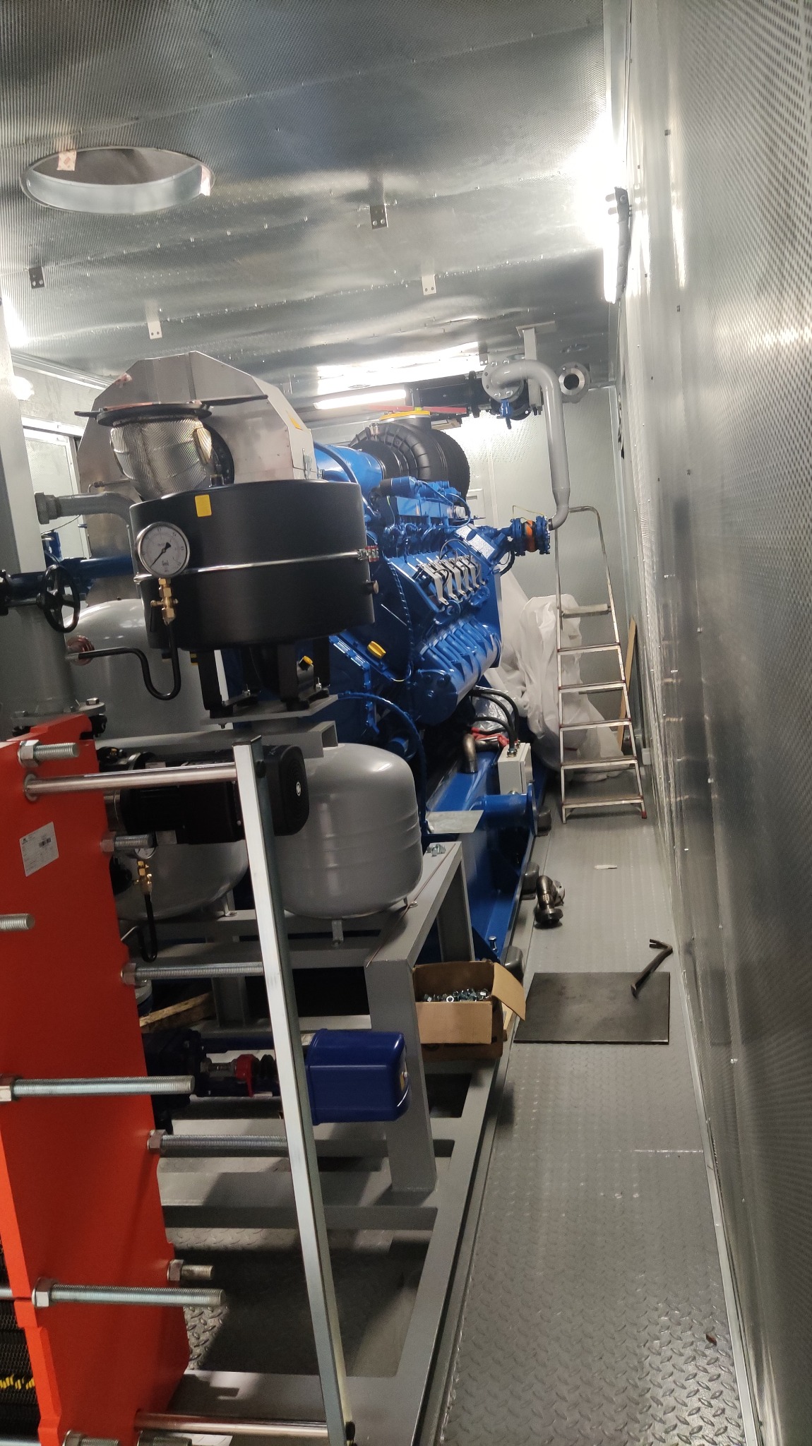 Wnętrze kontenera z zainstalowanym, niebieskim silnikiem spalinowym z osprzętem, widoczne manometry, rury, drabina i skrzynka z narzędziami.